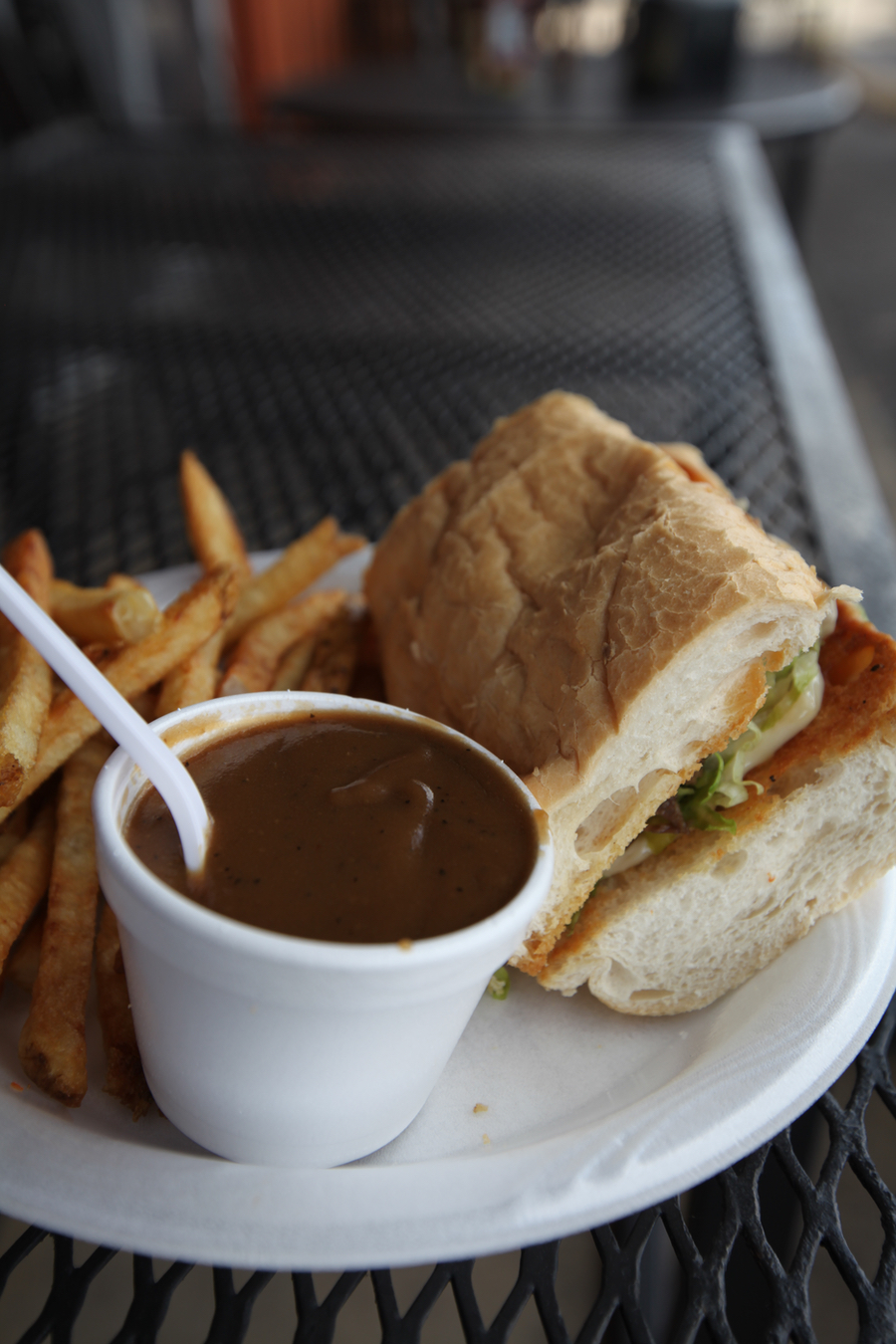 A photograph of a po' boy sandwich accompanied by a cup of dark brown gravy and fries