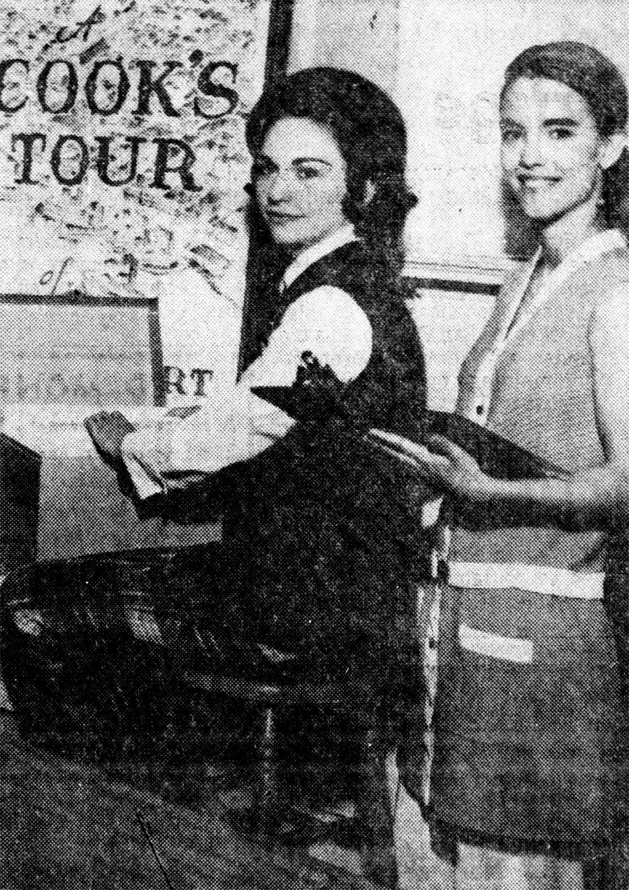 A black and white photo of two women working in an office, smiling into the camera